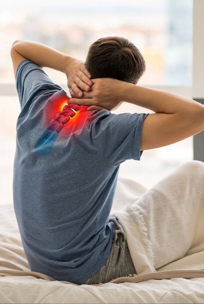 A person sitting on a bed holding their neck, illustrating neck pain with a highlighted red and blue spinal graphic on the back, symbolizing cervical discomfort. Relevant to Ayurvedic treatment for neck pain in Hyderabad with herbal therapy and yoga solutions.